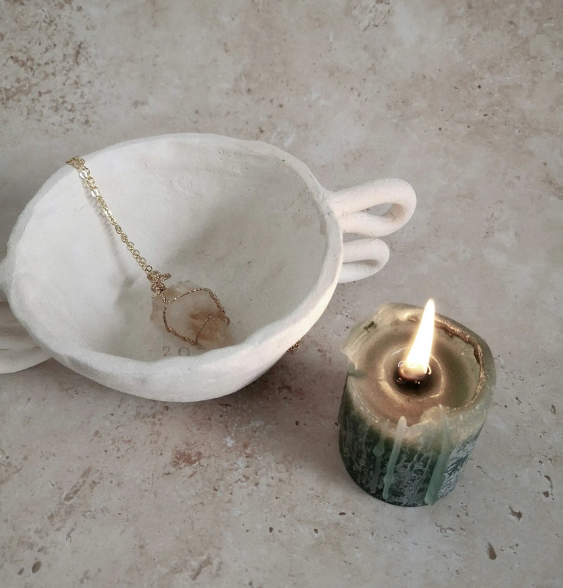 White ceramic cup with two handles and a gold chain necklace resting inside it.